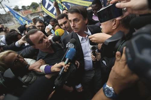 National Social Liberal Party presidential candidate Jair Bolsonaro talks to the press as arrives to campaign at the Madureira market in Rio de Janeiro, Brazil, Monday, Aug. 27, 2018. Brazil will hold general elections on Oct. 7. (AP Photo/Silvia Izquierdo)