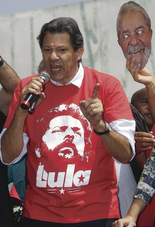 Brazil's presidential candidate for the Workers Party Fernando Haddad speaks to supporters during a campaign rally in Carapicuiba, the greater Sao Paulo area, Brazil, Thursday, Sept. 13, 2018. At right is a mask of jailed, former president Luiz Inacio Lula da Silva, who Haddad replaces as the party's candidate ahead of Oct. 7 elections. (AP Photo/Andre Penner)