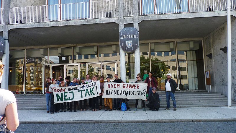Aktivister utanför Århus rådhus protesterar mot att stadens hamn ska byggas ut. ”Grön hamnutbyggnad? Nej tack” och “Vem gynnar hamn utbyggnationen” står det på banderollerna. Foto: Tuija Roberntz.