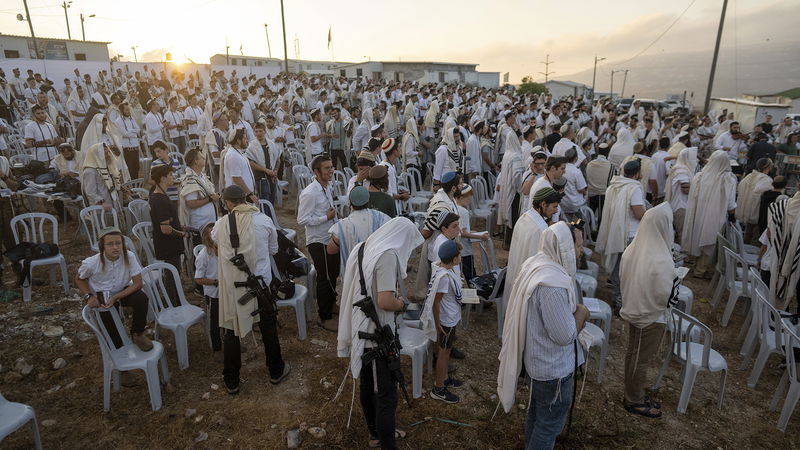 Beväpnade israeliska bosättare samlas för morgonbön på den ockuperade Västbanken. Foto: Ohad Zwigenberg/AP.