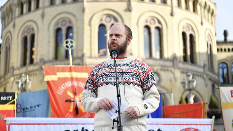 Mímir Kristjánsson talar framför fler än 100 fackföreningsfanor som samlats framför Stortinget i protest mot att höja pensionsåldern. Foto: Rodrigo Freitas/NTB/TT.