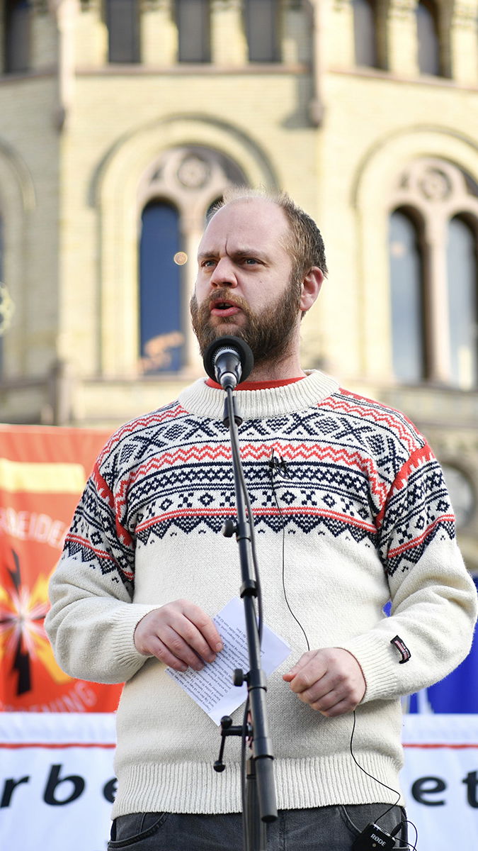 Mímir Kristjánsson talar framför fler än 100 fackföreningsfanor som samlats framför Stortinget i protest mot att höja pensionsåldern. Foto: Rodrigo Freitas/NTB/TT.