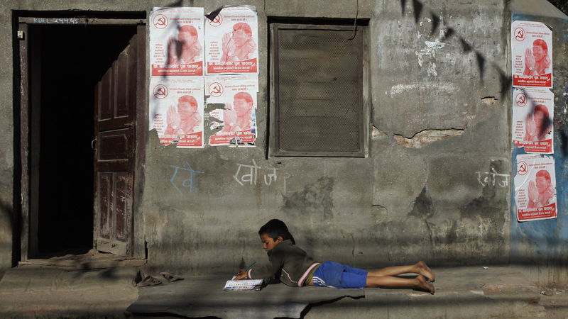 En nepalesisk pojke läser läxan framför en affisch för landets maoistparti. Foto: Niranjan Shrestha/AP/TT.