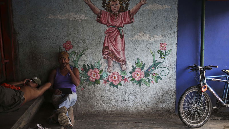 Cykelbud tar en rökpaus framför en mural med Jesusbarnet, i Masaya, Nicaragua. Foto: Esteban Felix/AP.