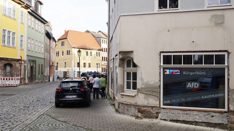 I ett skyltfönster syns reklam för Alternativ för Tyskland, och i bakgrunden skymtas det slitna huset Burg 19, en tidigare fristad för nazister. Foto: Mats O. Svensson.