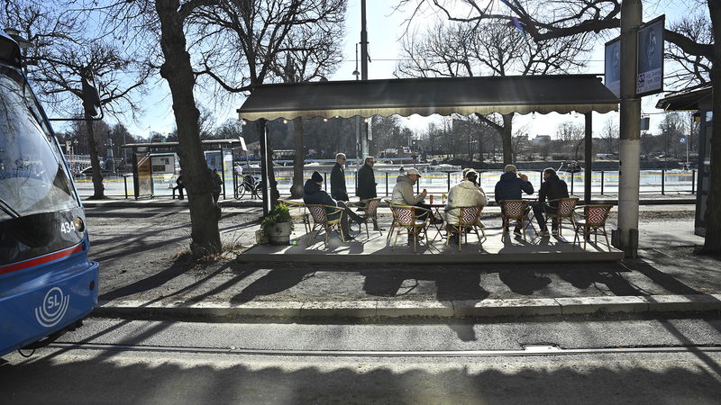 Människor sitter i vårsolen på en uteservering på Strandvägen i vårväder med sol och plusgrader. Foto: Fredrik Sandberg/TT.