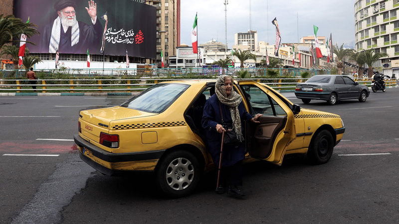 En kvinna stiger ur en taxi på en gata nära en affisch med Irans högste ledare ayatolla Ali Khamenei i Teheran den 2 mars 2026. Foto: AFP.